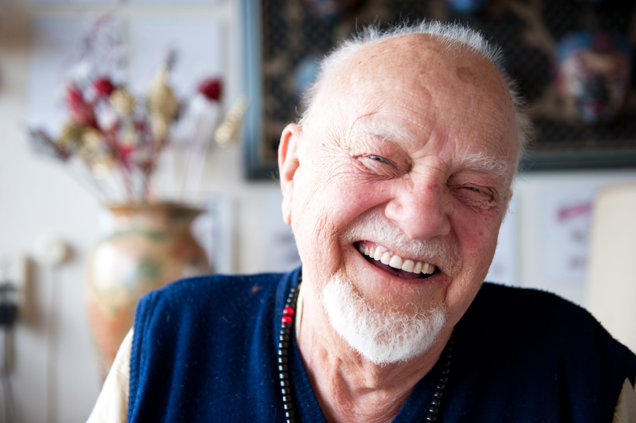 Elderly man laughing. Living room, vase with flowers.